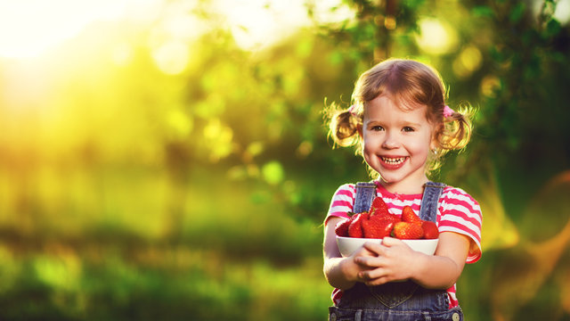 happy laughing child girl with ripe strawberry in summer on natu