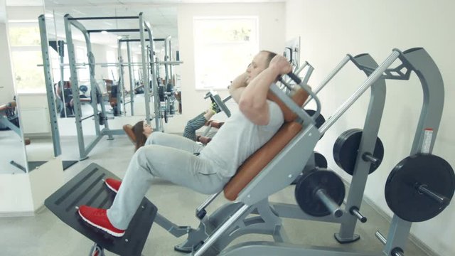 Couple working out in gym.Man in hack machine.woman doing leg press