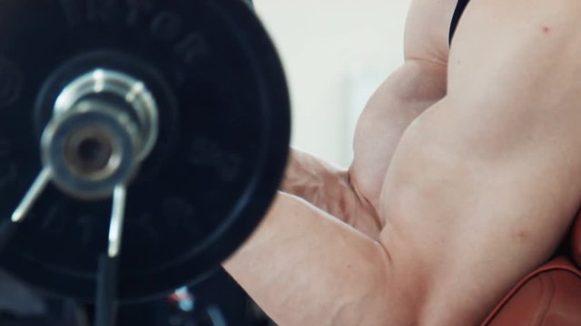 Unrecognizable muscular bodybuilder doing biceps exercise with heavy bar at scott bench