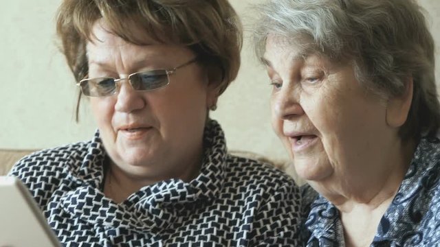 Two elderly women watch pictures using a tablet