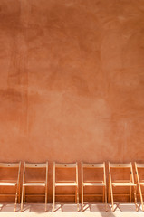 empty wooden chairs against orange cement wall