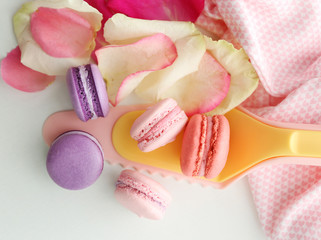 Fresh macaroons and rose petals on white background