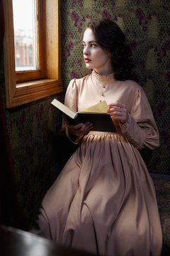 Young woman in beige vintage dress of early 20th century reading