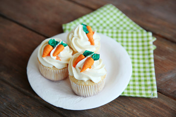 Cupcakes with frosting and decorative carrots on wooden background