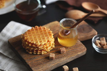 Tasty waffles with honey on cutting board