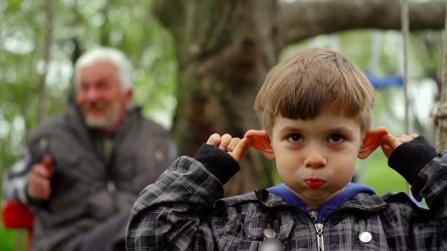 Young Boy With His Grandfather Enjoying Outdoors And Making Faces
