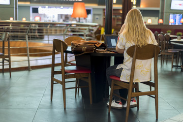Blond girl working on laptop in stylish restaurant