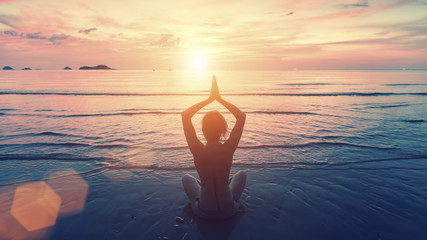 Silhouet jonge vrouw die yoga beoefent op het zonsondergangstrand. Rust en concentratie.