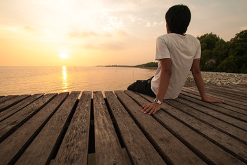 Young man relax siting on pier looks forward with sunset sky