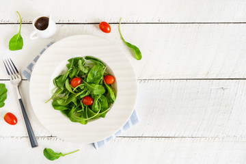 Rocket salad with cherry tomatoes on white wooden background