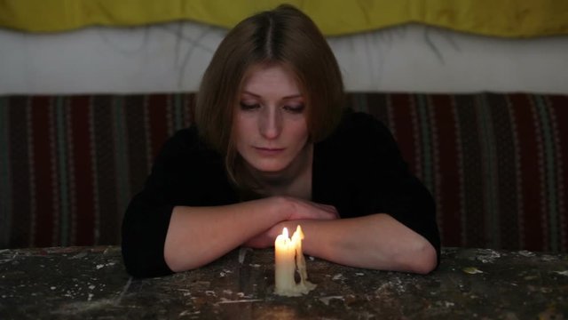 Depression. Young sad woman sitting with a candle on the table, gloomily looking into the camera