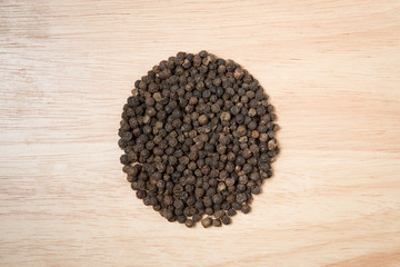 pile of black dried pepper on a wood background