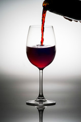 Red wine being served into a glass cup on a white background wit