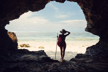 Silhouette of young woman standing in cave on the beach and looking far away