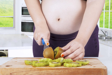 Expectant woman slicing kiwi fruits