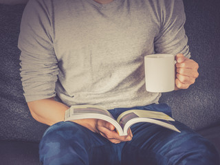 Obraz premium Man reading book, holding coffee cup, vintage filter