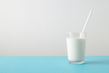 Transparent glass with fresh organic milk and white drinking straw inside isolated on pastel blue table Space for your text above 