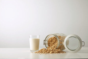 Transparent glass with fresh organic milk near lying full opened rustic jar with rolled oats spread...