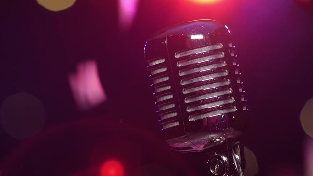 Vintage shiny microphone reflects glitter confetti against blurry flashing lighting