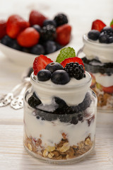 Healthy yogurt dessert with muesli, strawberries, blackberries and  blueberries on white wooden table.