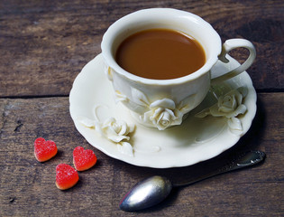 Сoffee with milk in vintage porcelain cup and marmalade heart sugar sweets on old wooden background. Selective focus.