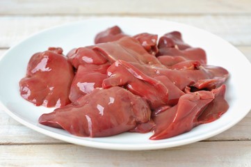 Raw liver on the white plate on the wooden background