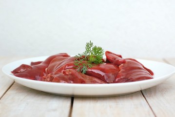 Raw liver on the white plate on the wooden background