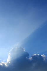 sunbeam of sunlight through clouds on clear blue sky