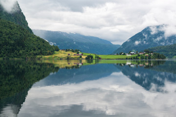 Landscape with lake and rural land with colored houses, mirror reflection of the mountains in the water, Norway