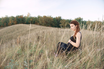 Naklejka na ściany i meble Pregnant woman in black dress and dreadlocks on the background of wild nature