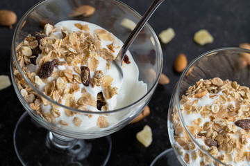 Granola with yoghurt, nuts and fruits in glass bowl on dark background. Delicious, healthy sweet dessert for breakfast. Cereal, muesli. Copy space, closeup.