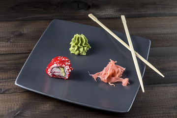 Sushi. Tobico roll with pickled ginger and wasabi with sushi sticks served on grey plate on wooden table.