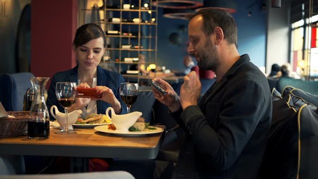 Happy couple taking photos with cellphone of their meal sitting in cafe 

