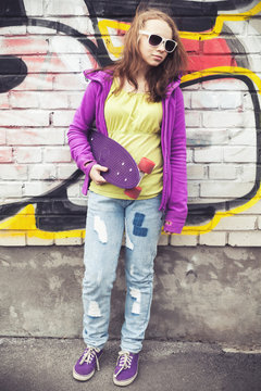 Blond teenage girl holds skateboard, vertical photo