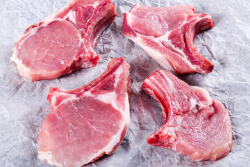 Raw fresh pork chops on a white parchment paper, top view