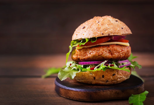 Big sandwich - hamburger with juicy chicken burger, cheese, tomato, and red onion on wooden background