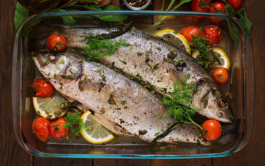 Two baked seabass in a baking dish with spices on an wooden background. Top view