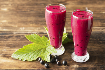 Two glass glasses with black currant smoothie on a dark wooden background