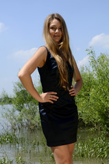 Junge hübsche Frau mit langen braunen Haaren in blauen Minikleid an Flussufer