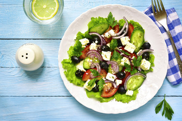 Traditional greek salad on a white plate over rustic wooden back