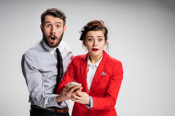 Business concept. The two young colleagues holding mobile phone on gray background