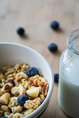 Close view of healthy breakfast on a wooden table. Muesli in a white bowl. Oats with nuts and blueberries. Glass of milk. Vertical view. Selective focus.