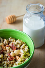 Close view of healthy breakfast on a wooden table. Muesli in a green bowl. Oats with nuts and blueberries. Glass of milk. Vertical view. Selective focus.