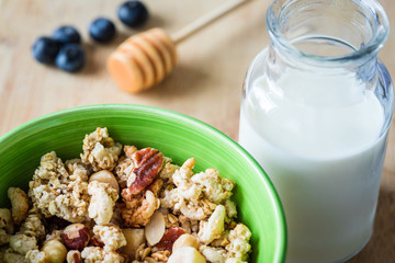Close view of healthy breakfast on a wooden table. Muesli in a green bowl. Oats with nuts and blueberries. Glass of milk. Horizontal view. Selective focus.