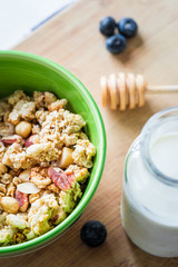 Close view of healthy breakfast on a wooden table. Muesli in a green bowl. Oats with nuts and blueberries. Glass of milk. Vertical view. Selective focus.