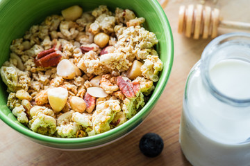 Close view of healthy breakfast on a wooden table. Muesli in a green bowl. Oats with nuts and blueberries. Glass of milk. Horizontal view. Selective focus.