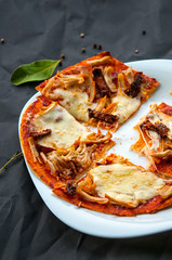 Home made thin fresh italian pizza served on white plate and black background