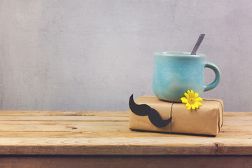 Coffee cup and gift box with paper mustache on wooden table. Father's day holiday concept