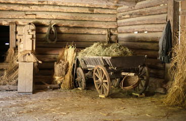 Wooden cart with hay in old barn. - obrazy, fototapety, plakaty