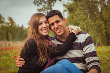 Fototapeta premium Young couple sitting on the grass in a field of red poppies and
